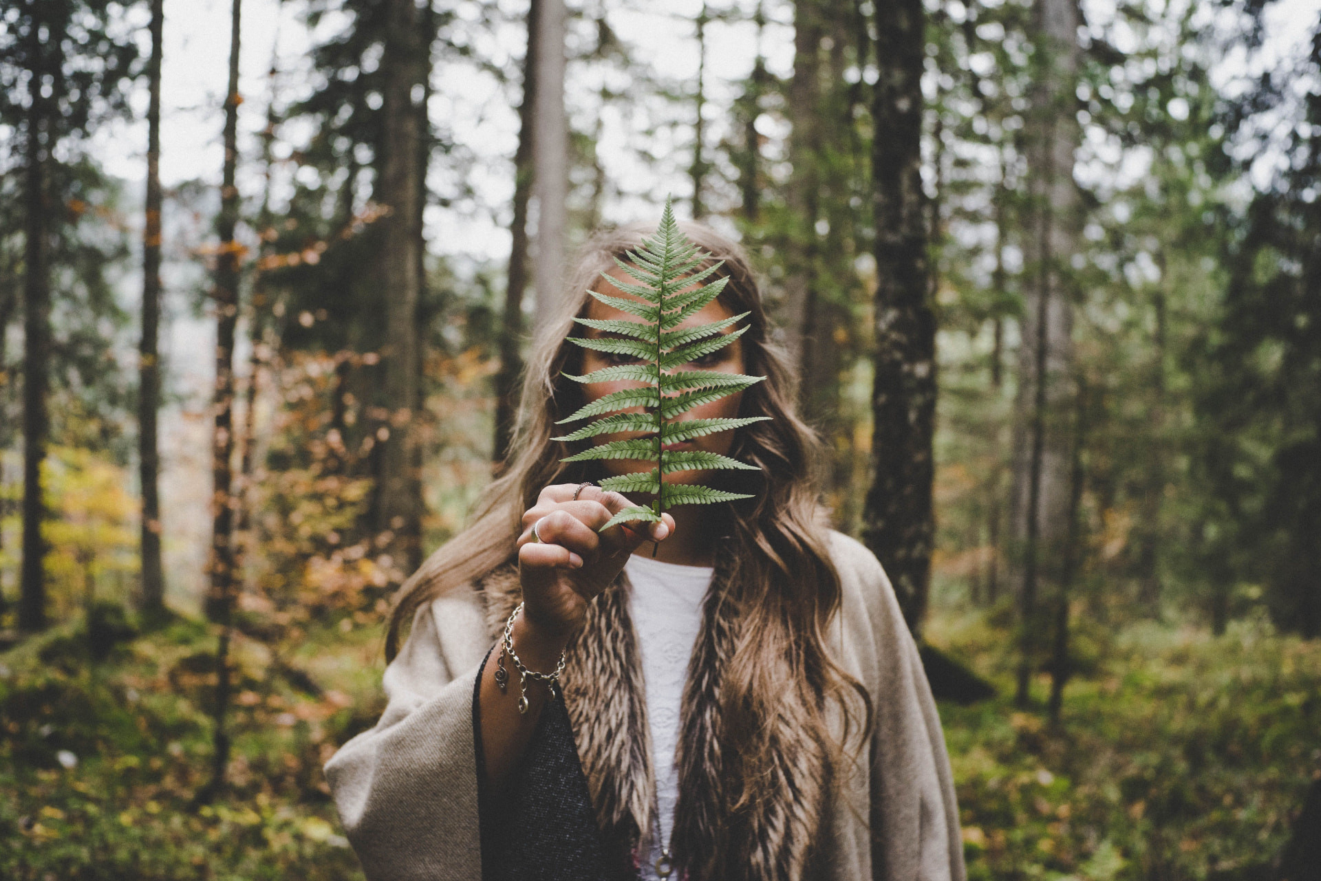 A woman in a forest holding a fern leaf in front of her face.