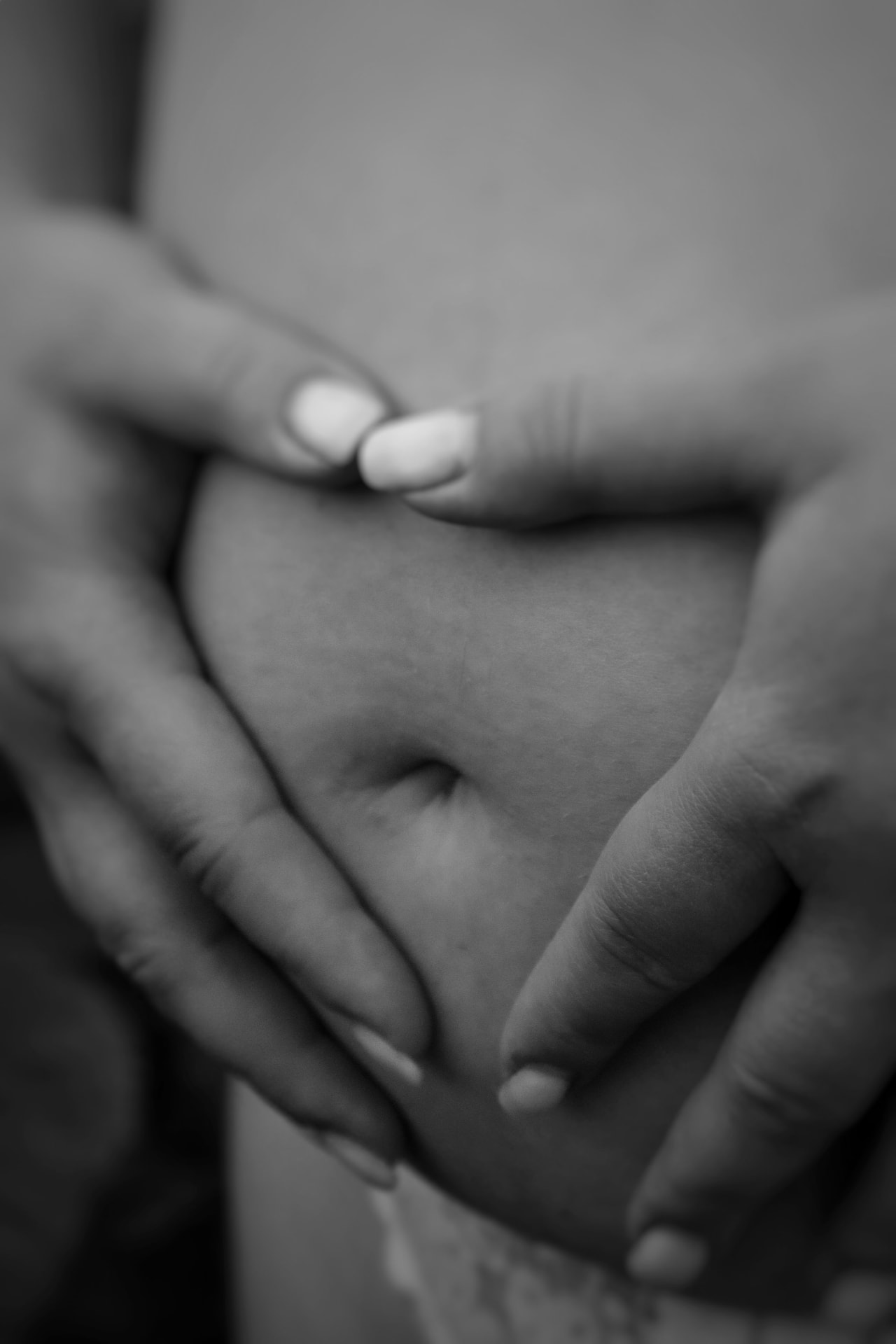 Black-and-white close-up of two hands forming a heart shape around a bare belly.