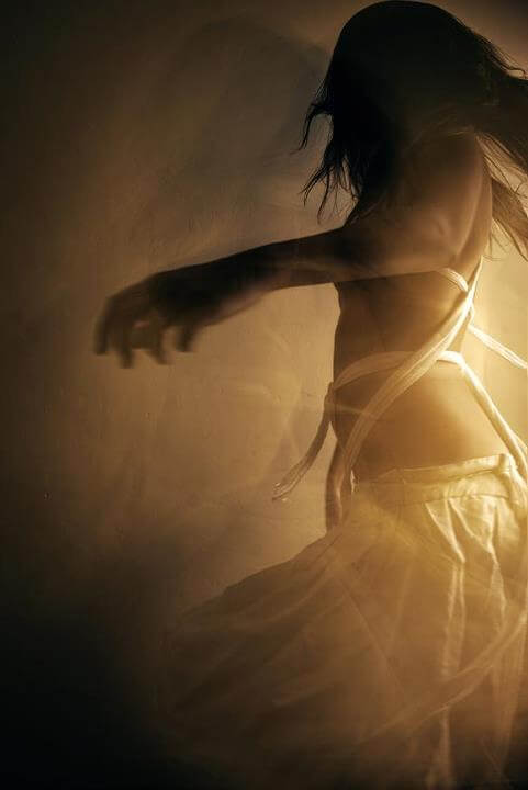 A woman dancing, seen from behind in soft warm light, her white dress catching the glow