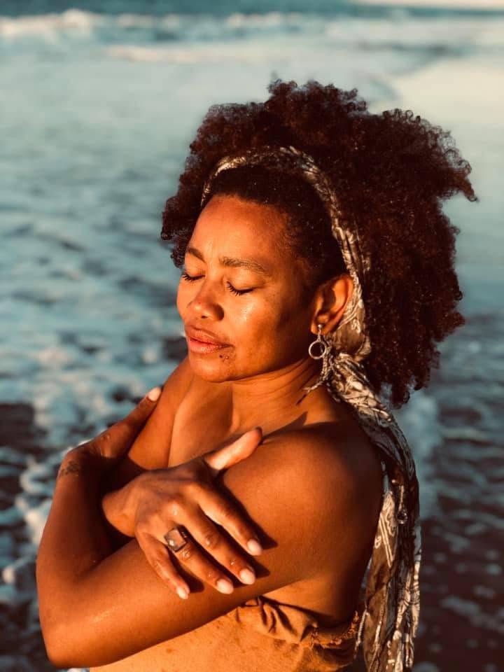 A woman with closed eyes embracing herself on the beach in golden light